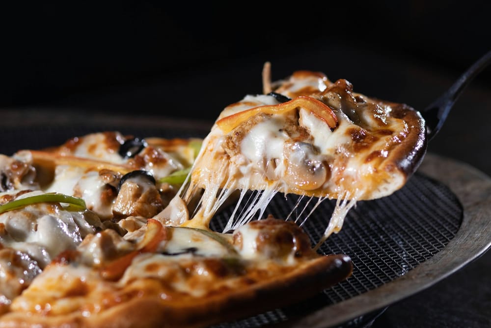 Ein Stück Pizza mit langen Käsefäden wird mit dem Pizzaheber gehoben